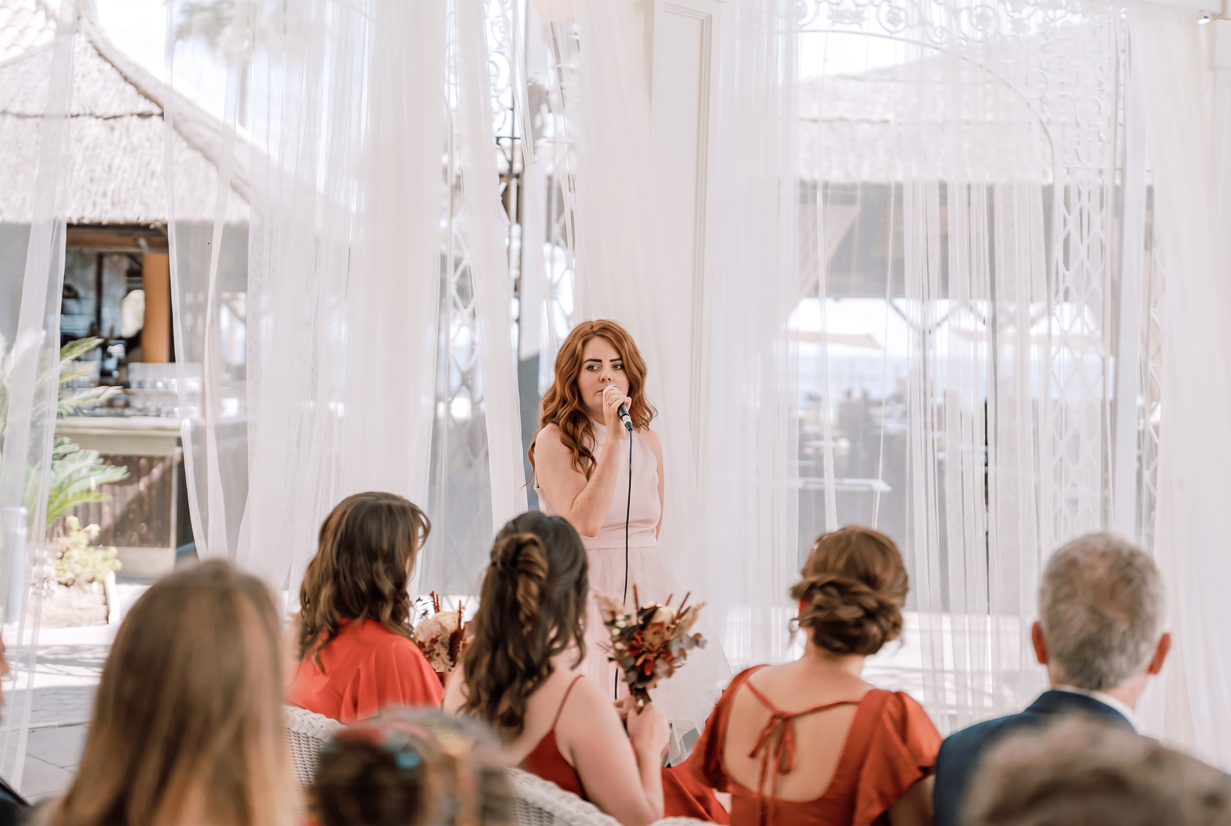 Aimée Ní Riordáin singing sean-nós acapella at a wedding ceremony, surrounded by sheer white drapes and seated guests